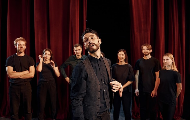 Foto ragazzo espressivo che pratica il suo ruolo gruppo di attori in abiti di colore scuro durante le prove a teatro