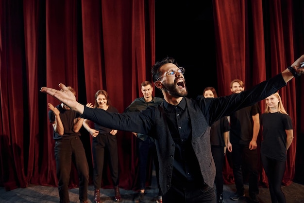 Expressionalible guy practicing his role Group of actors in dark colored clothes on rehearsal in the theater