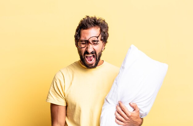 Expressive crazy man shouting aggressively, looking very angry and holding a pillow