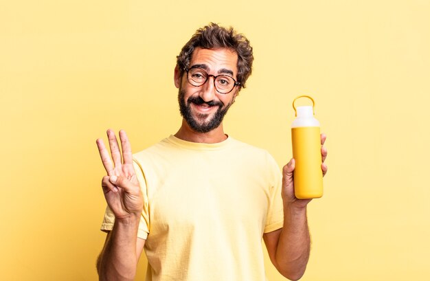 Expressive crazy man smiling and looking friendly, showing number three with a tea thermos