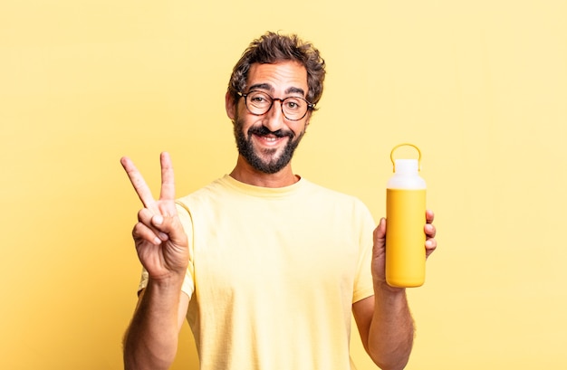 expressive crazy man smiling and looking happy, gesturing victory or peace with a tea thermos