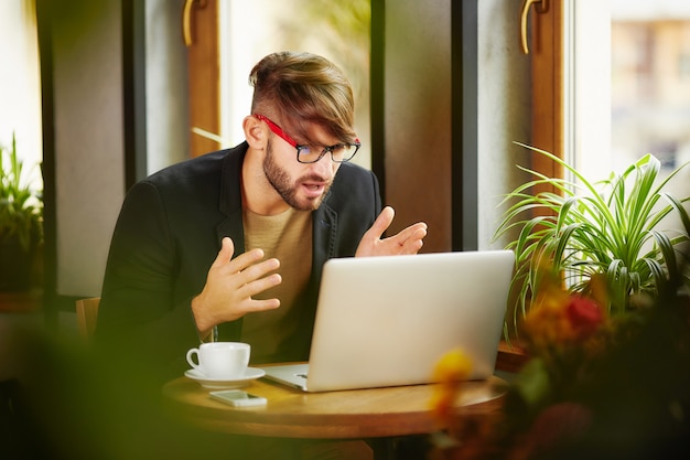 Expressive man sitting at laptop in cafe