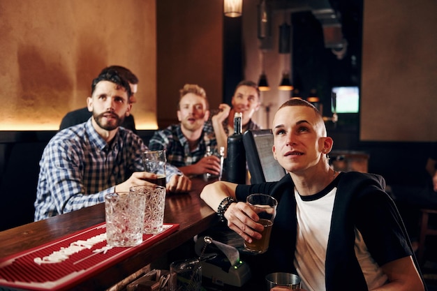 Expressive people watching soccer group of people together\
indoors in the pub have fun at weekend time