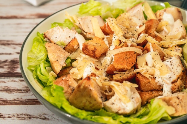 Exquisite Caesar salad with small bites of chicken and a traditional aioli sauce in a small bowl on a rustic table High view Closeup detail Gourmet concept