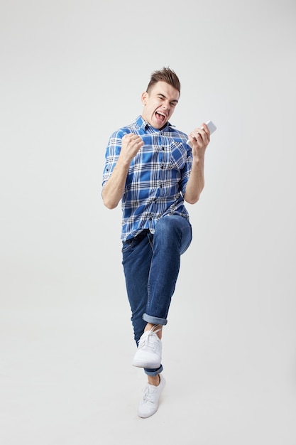 extatisch vol energie kerel gekleed in een geruit overhemd en jeans houdt mobiele telefoon