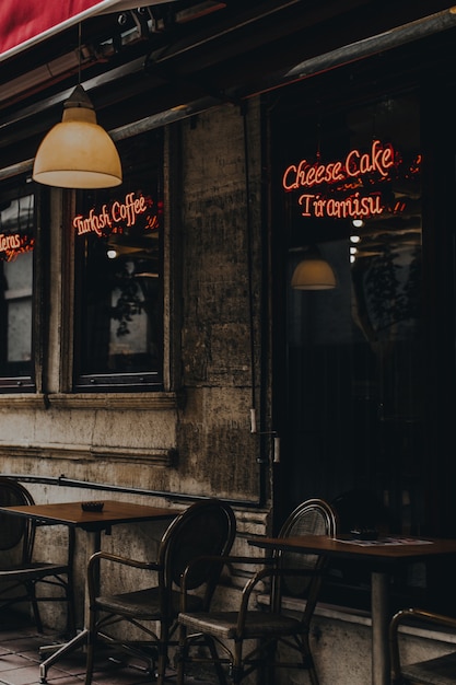 茶色の木製のテーブルと椅子、赤いネオンサインのある居心地の良いトルコのカフェの外観とベランダ。ストリートスタイル。