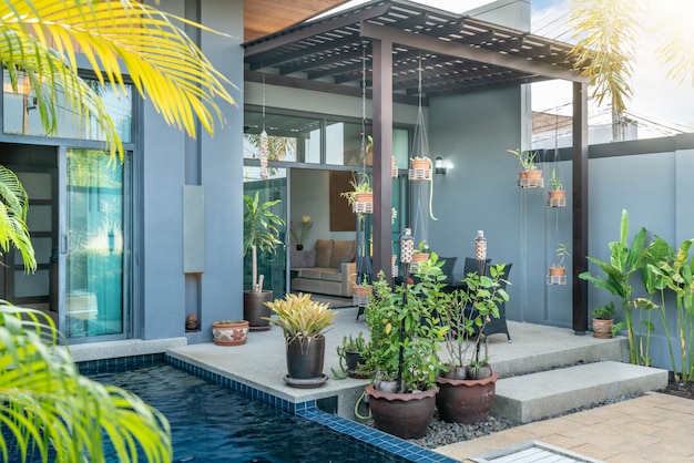 태양 침대와 푸른 하늘과 녹색 정원이있는 열대 수영장 빌라를 보여주는 외부 및 인테리어 디자인