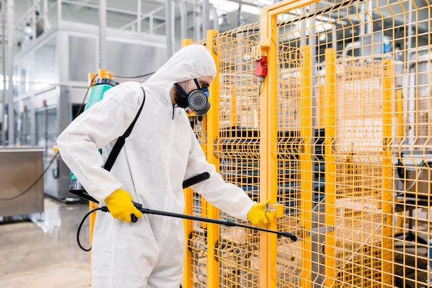 Exterminator in industrial plant spraying pesticide with sprayer