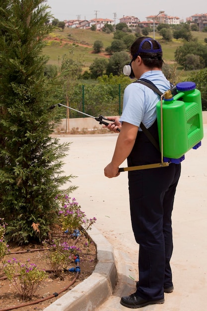 Sterminatore in abbigliamento da lavoro che spruzza pesticidi con spruzzatore