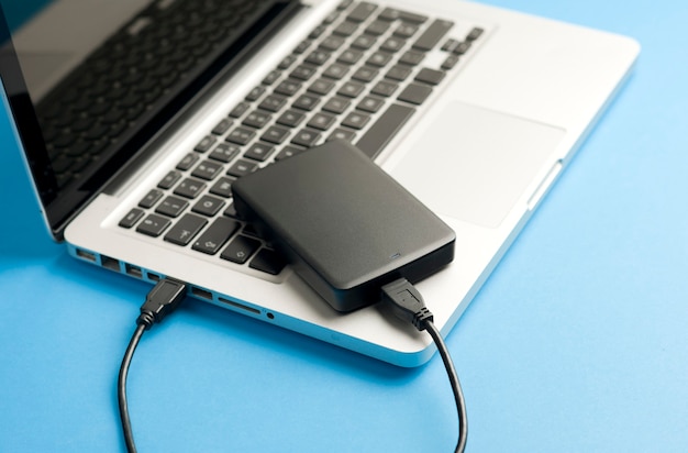 External hard disk black  with cable usb partial view of laptop on the blue office table Top view