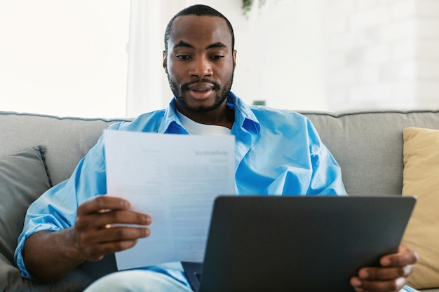 Externe carrière freelance baanconcept Jonge afro-amerikaanse man die laptopcomputer gebruikt en door documenten kijkt