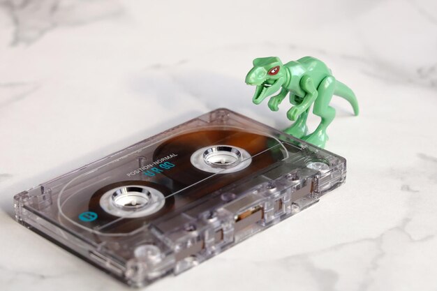 Extinct audio cassette outdated technology small green dynazaur looks opening his mouth