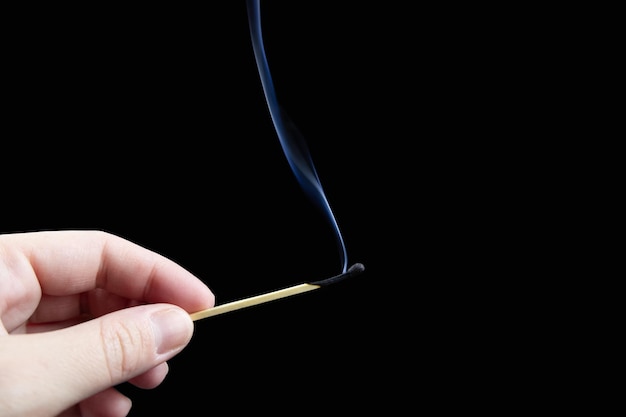 Extinguished match with blue plume of smoke in fingers on black background