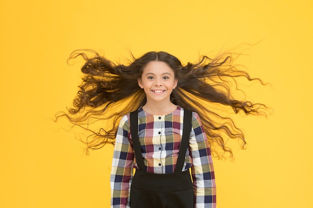 Extra licht. Lucht in haar haar. natuurlijke schoonheid. Meisje jongen lang haar vliegen in de lucht. Kind met natuurlijke mooie gezonde haar gele achtergrond. Tips voor gezond haar. Kapsalon. Schoonheidsprocedure.