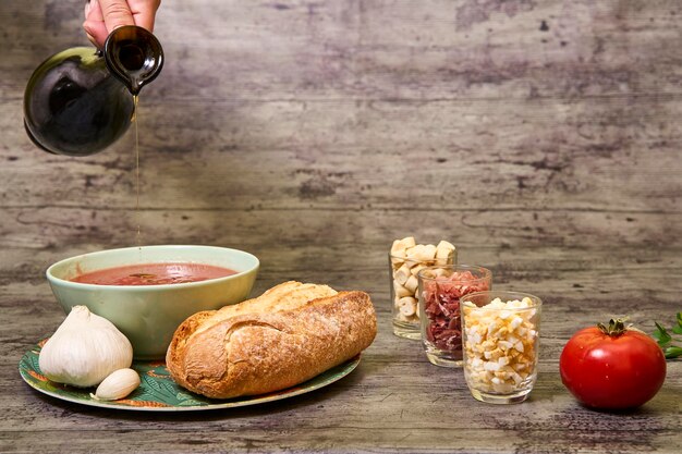 Extra virgin olive oil being served with andalusian gazpacho in a bowl accompanied by bread and garlic and on the right are croutons egg and serrano ham and a tomato concept of mediterranean food