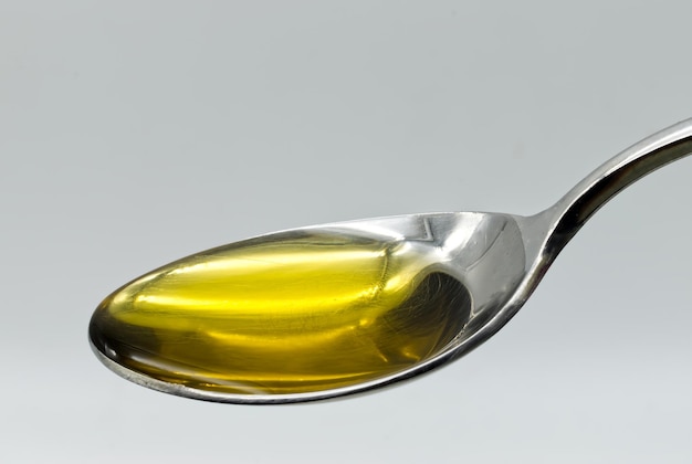Foto olio d'oliva vergine extra in un cucchiaio d'argento isolato su sfondo bianco