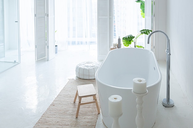 Extra white and very light minimalistic stylish elegant interior of bathroom with modern bath, green plants and wooden elements