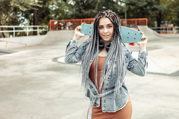 Extraordinary female millennial skater with colorful makeup African braids in a skate park Youth lifestyle concept