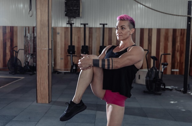 Extraordinary muscular powerful woman with pink hair is practicing warm-up before intense workout in a modern cross-gym.