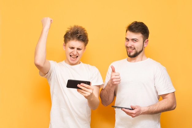 Extreme boys emotionally play games on smartphone, stand on yellow