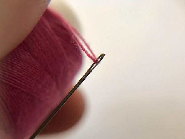 Photo extreme close-up of hand holding pink thread and sewing needle against white background