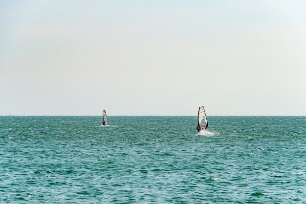 エクストリームマンアスリートは、青い海と地平線に対する海の波のウィンドサーフィンで泳ぎます 水に赤い帆のエクストリームウォータースポーツの動き 海での夏の楽しみ