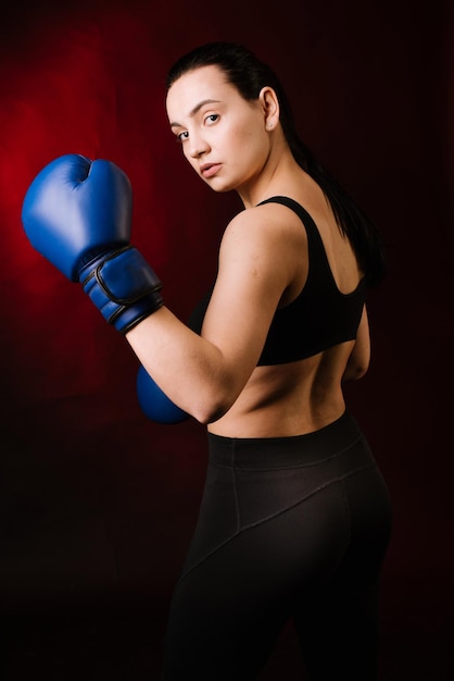 濃い赤の背景に青いボクシンググローブを身に着けているエクストリームスポーツの女性ボクサー