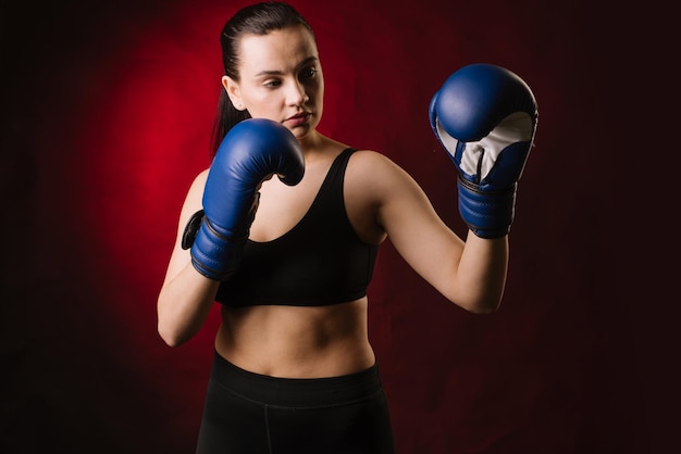Extreme sportvrouwenbokser die blauwe bokshandschoenen draagt op donkerrode achtergrond