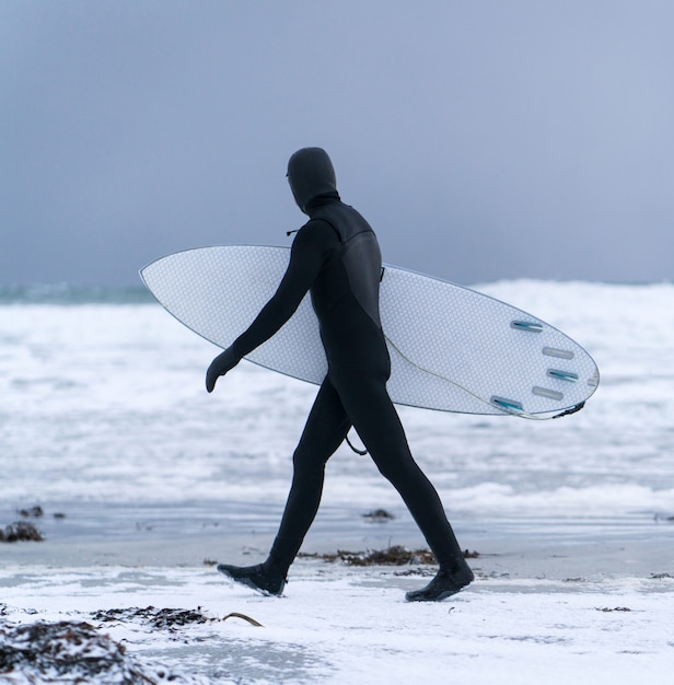 Foto surfista estremo che cammina sulla spiaggia della neve di inverno