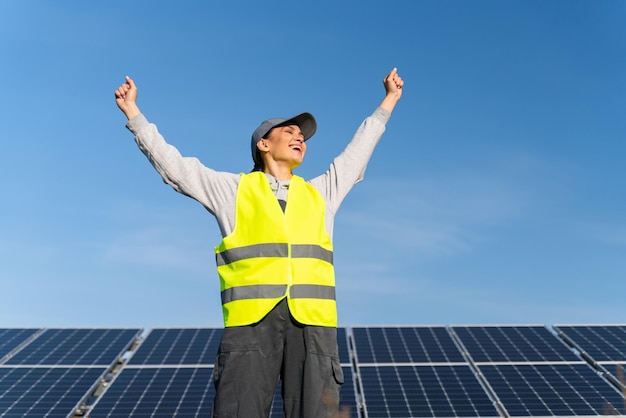 Donna eccitata estremamente felice che indossa l'uniforme che apre ampiamente le mani e urla sentendosi libertà mentre lavora nella fattoria dei pannelli solari