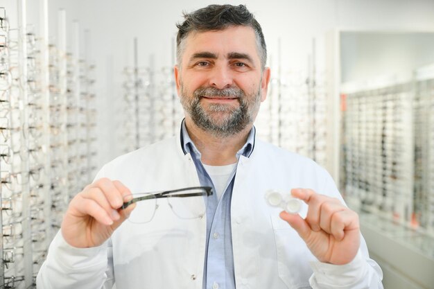 Eye doctor choosing between eyeglasses and lenses standing in front of the eye chart in the cabinet