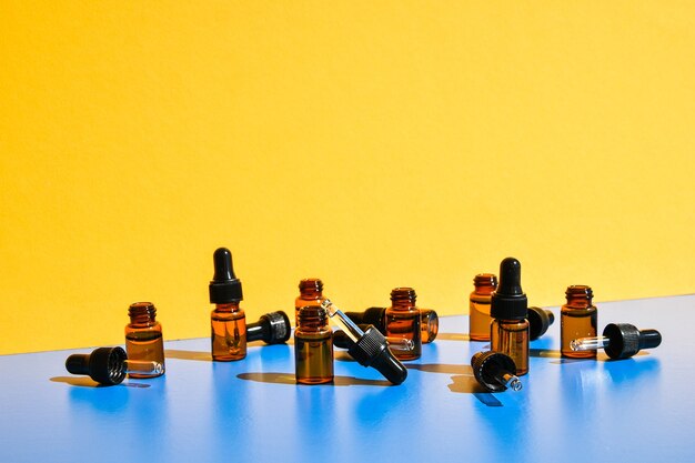 Eye dropper bottles with dark shadows on yellow and blue background. Modern creative minimalism concept. Copy space