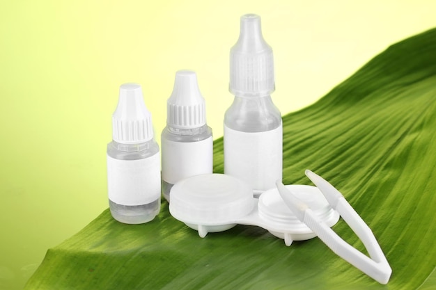 Eye drops and lenses on leaf on green background