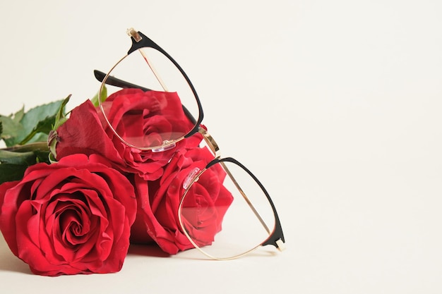 Eye glasses and red roses on beige background