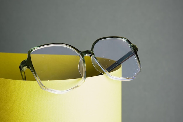 Foto occhiali da vista su carta arrotolata, sfondo geometrico, colori verdi, sfondo grigio, concetto di test della vista, bellissimi accessori moda alla moda nel negozio di ottica