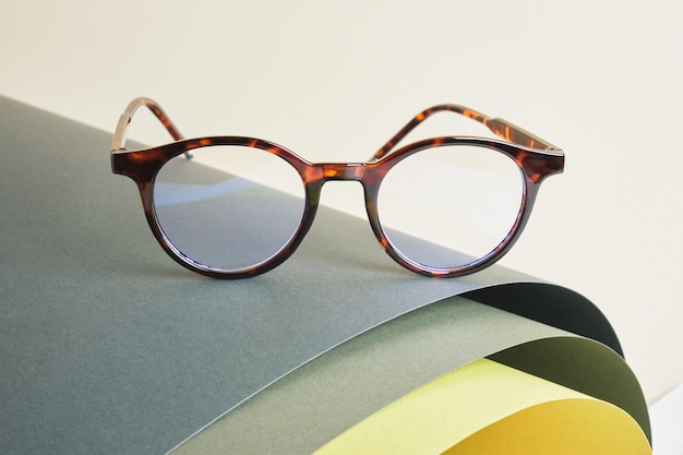 eye glasses on rolled paper, geometric background, green colors, gray background, vision test concept, beautiful stylish fashion accessories in optics store