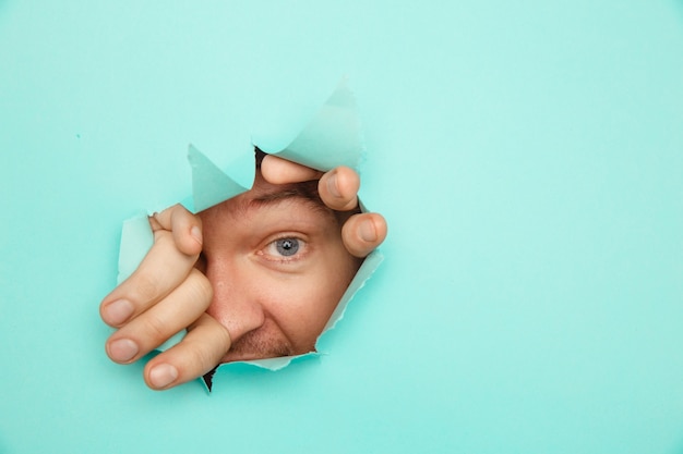 Eye looking through hole in paper. Man looking through hole in blue paper.