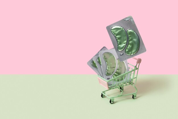 Eye patches in shopping cart on green backgound face care beauty treatment concept