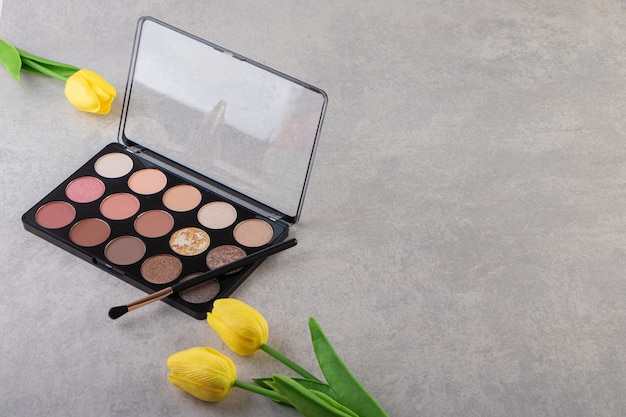 Eye shadow cosmetics with brush and yellow tulips.