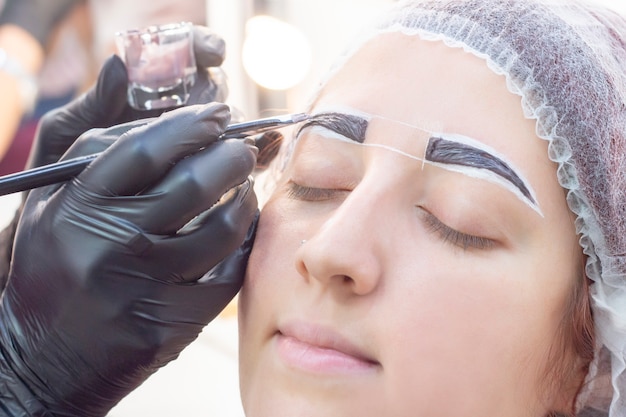 Eyebrow dyeing. beauty saloon. the girl lies with her eyes closed on the eyebrow dyeing procedure. The eyebrow master applies brush to the eyebrows of the client.