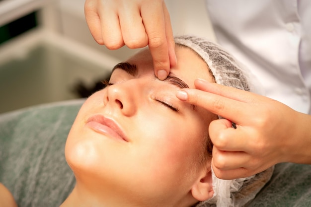 Eyebrow massage Beautiful caucasian young white woman receiving an eye and eyebrow massage with closed eyes in a spa salon