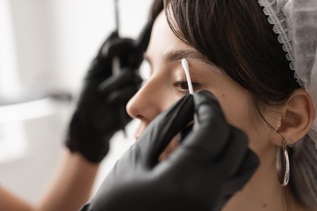 Eyebrow master erases the contour after the procedure with a cotton swab