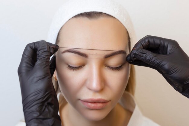 Eyebrow tattooing permanent eyebrow makeup master applies the contour with thread on the clients