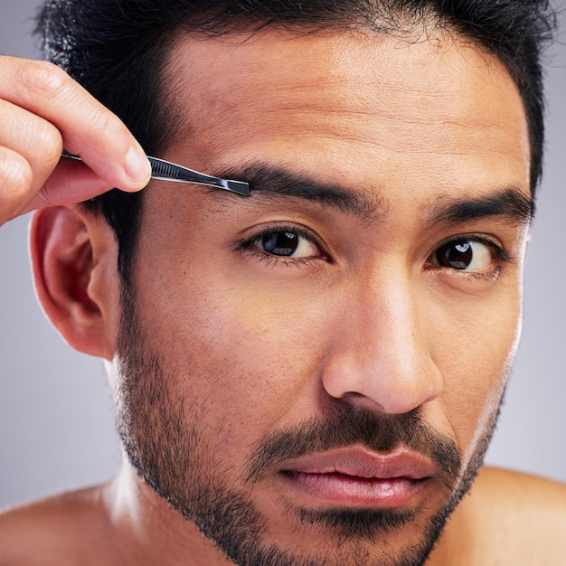 眉毛ピンセットと美容衛生やグルーミングのためのスタジオの男性の肖像画脱毛脱毛と灰色の背景にスキンケアセルフケアや化粧品ツールのための深刻なアジア人の顔