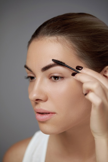 Eyebrows shaping. portrait of beautiful girl with brow pencil.\
close-up of young woman with professional makeup