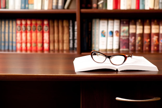 Eyeglasses lying on the opened book and many other books on background