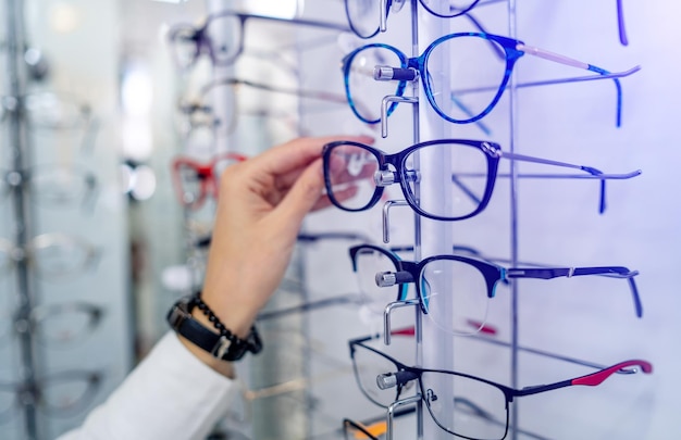 Eyeglasses shop Stand with glasses in the store of optics Woman's hand chooses glasses