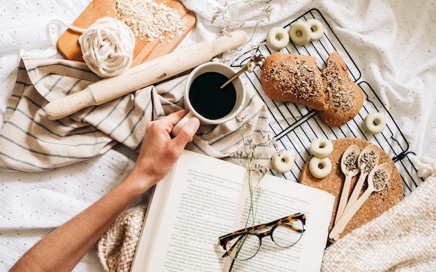 Occhiali sulla cima di un libro intorno al cibo e una mano che tiene una tazza di caffè