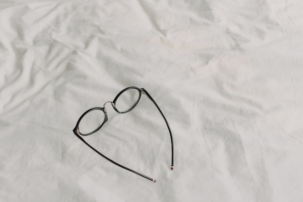 Eyeglasses with black plastic temple on white bed sheet.