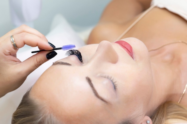 Eyelash extension procedure. Beautiful woman with long eyelashes in a beauty salon. Eyelashes close up. brush in hands